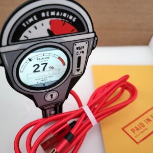 Griftmeter Parking Meter shell in its shipping box with the dial lit and showing a live reading, beside the envelope, stand and red cable