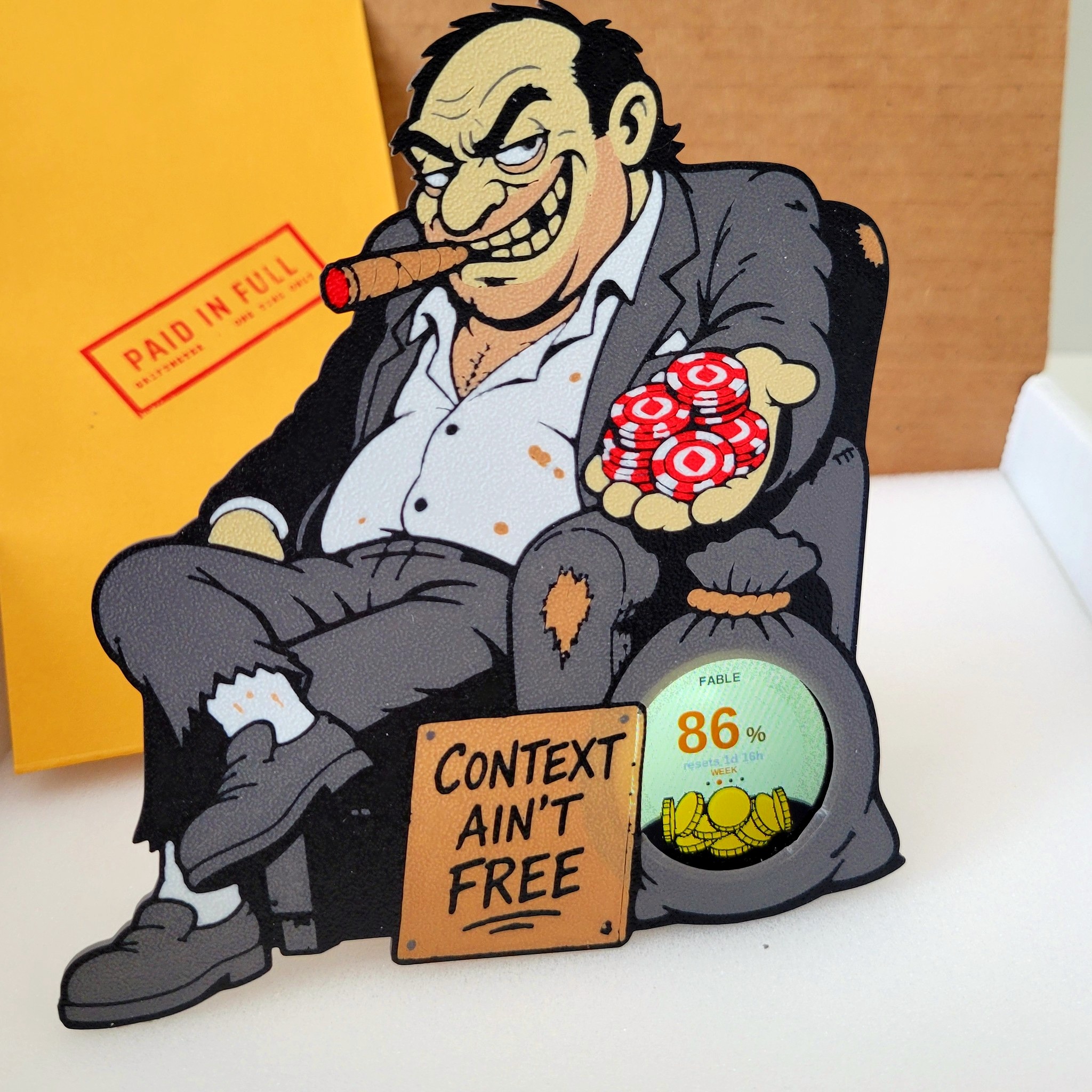 Griftmeter Starter Bundle: the dial lit inside the Grifter shell, standing on its stand in front of the box and envelope