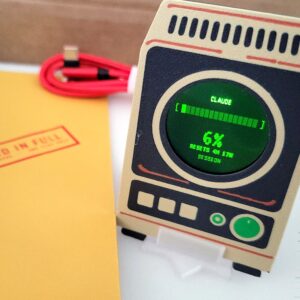 Griftmeter Starter Bundle: the Terminal shell on its stand in the box, screen lit and reading Claude usage, beside the envelope and red cable
